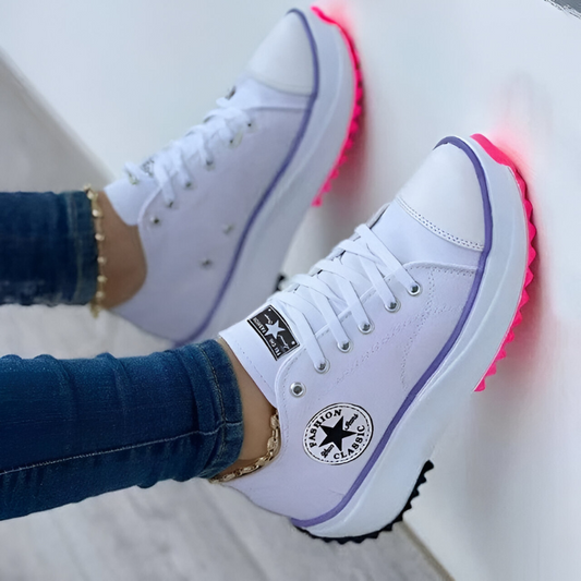 Zapatillas ortopédicas blancas con borde lila y suela fucsia, cordones y parches.