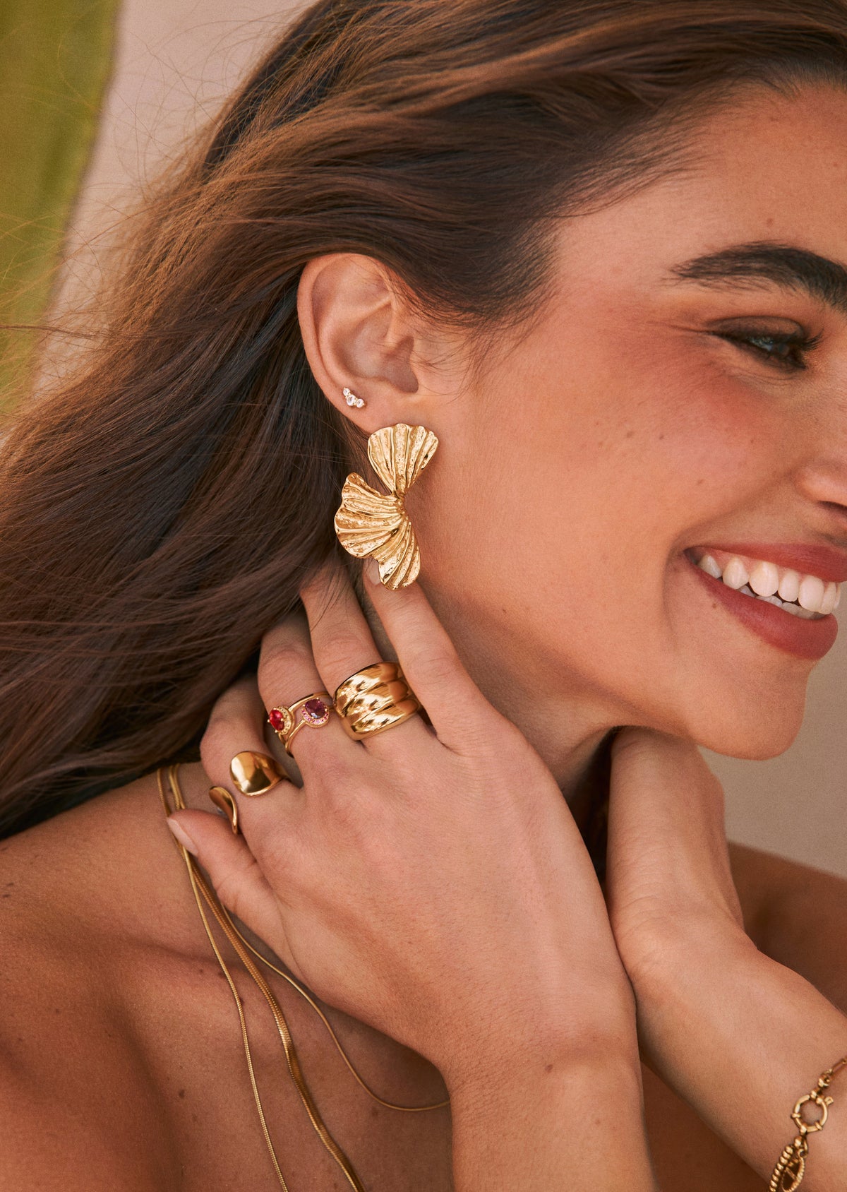 Anillo dorado con gema roja ovalada y brillo alrededor, en mano junto a otras joyas