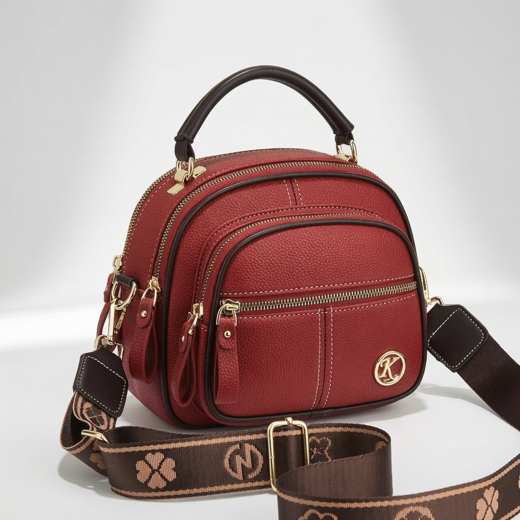 Bolso bandolera compacto de cuero rojo con cierre, correa estampada y placa circular K.