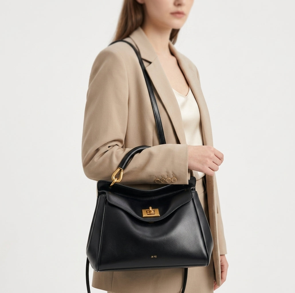 Bolso de piel lisa negro con asa y bandolera, solapa frontal con cierre metálico.