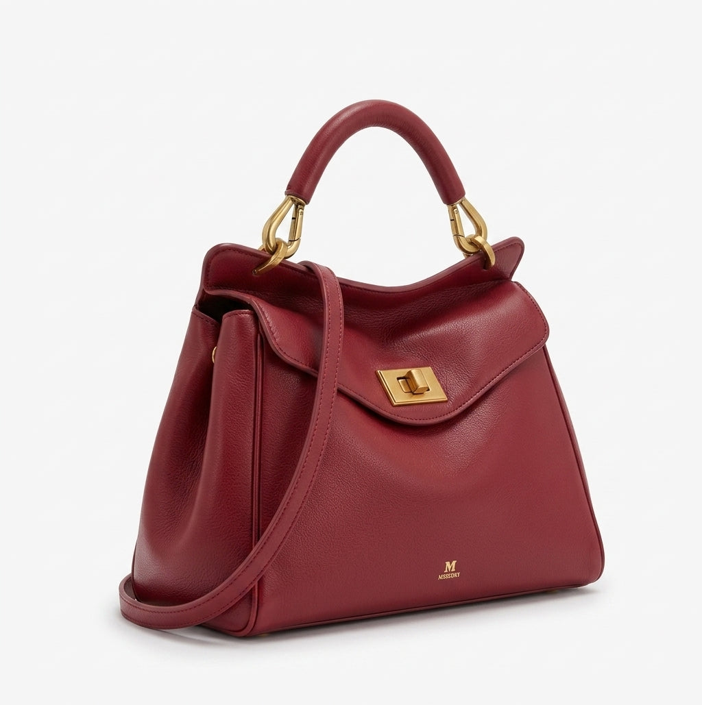 Bolso de piel lisa granate con asa doble y bandolera, solapa frontal con cierre metálico.